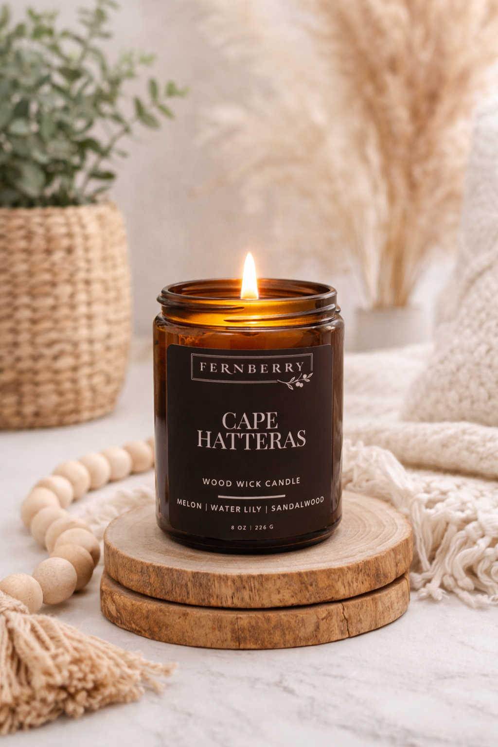 Fernberry Cape Hatteras candle on a wooden coaster with decorative elements in the background