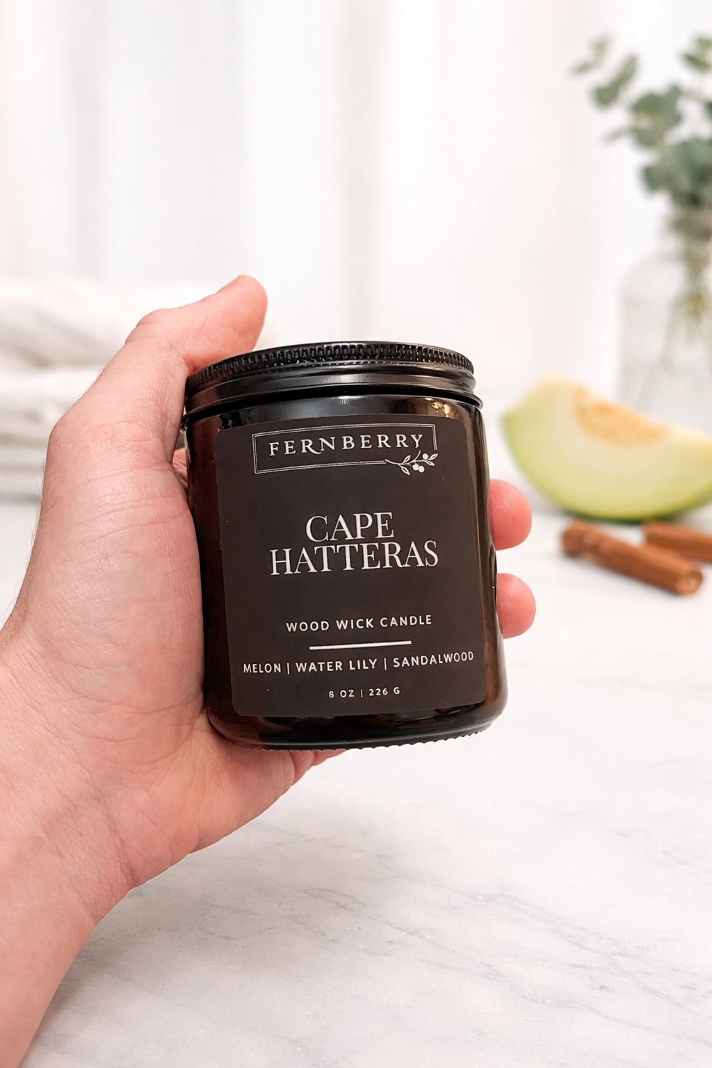 Hand holding a Fernberry Cape Hatteras candle with a blurred background