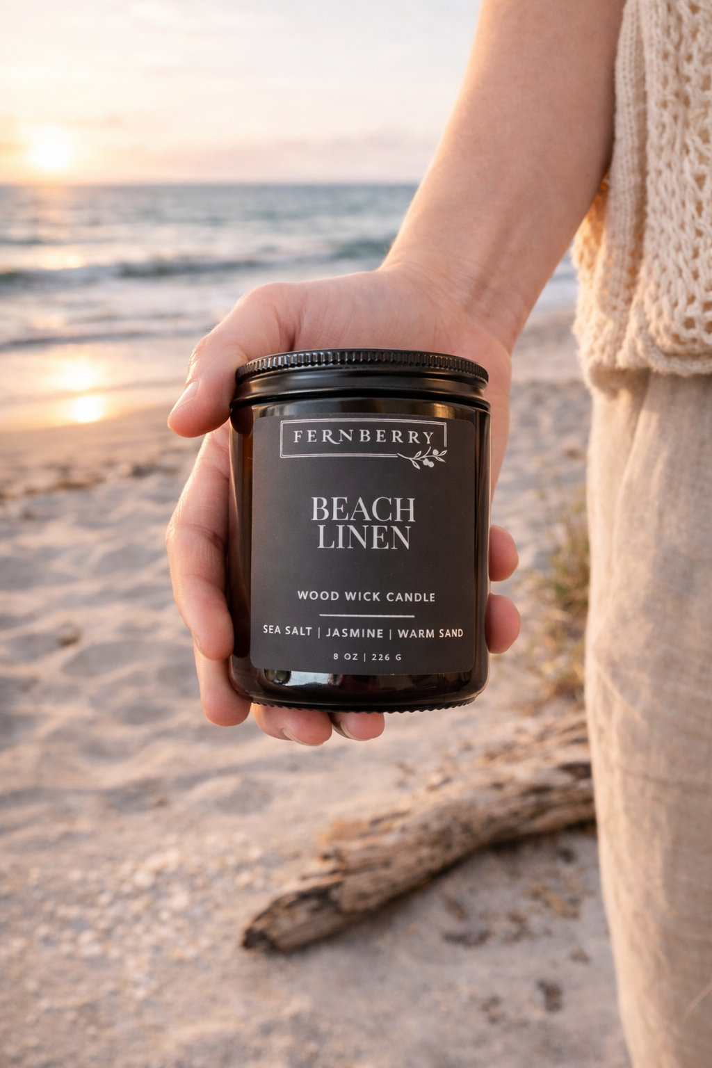 Person holding a Fernberry Beach Linen candle on a beach at sunset