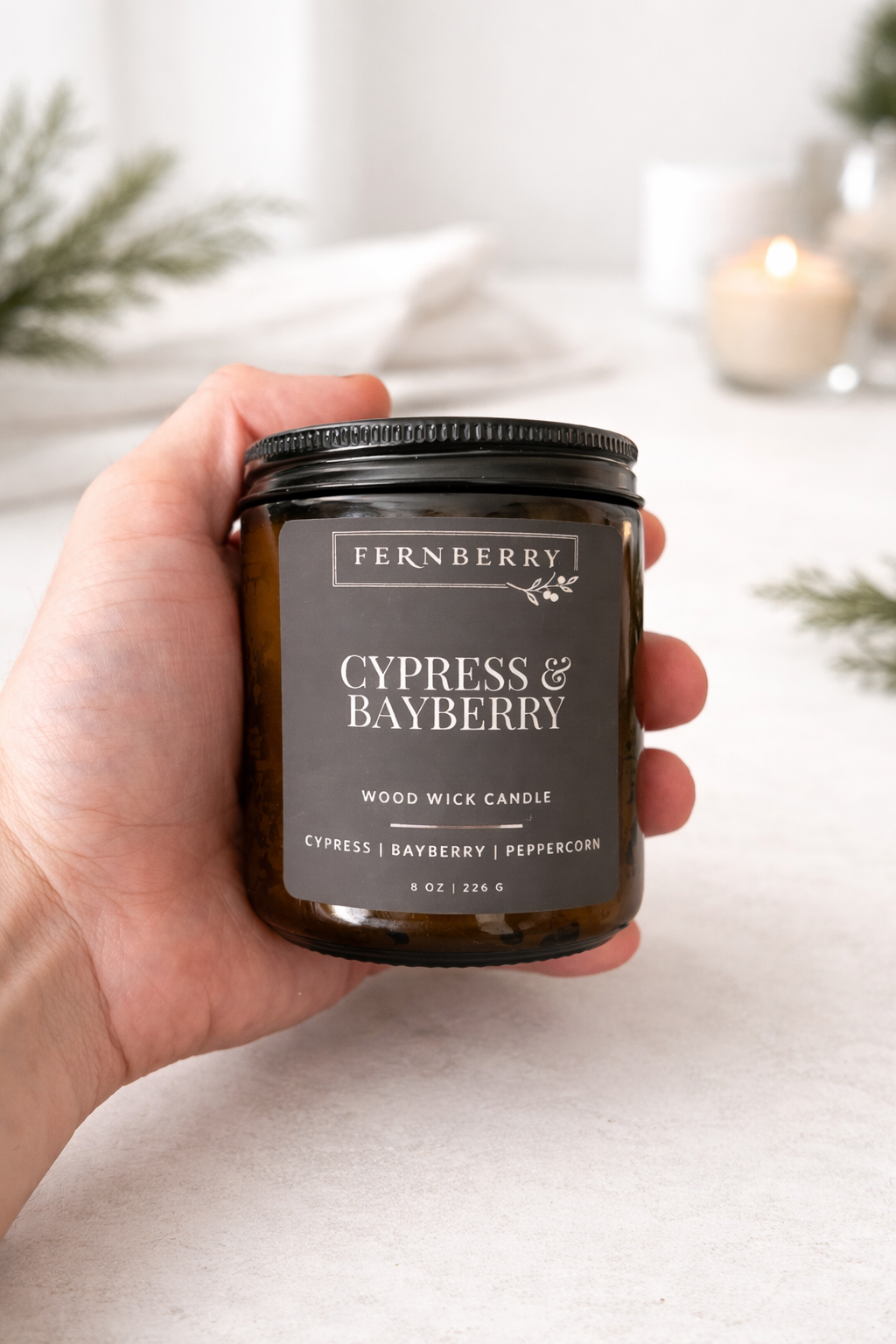 Fernberry Cypress & Bayberry candle held in a hand with a blurred background