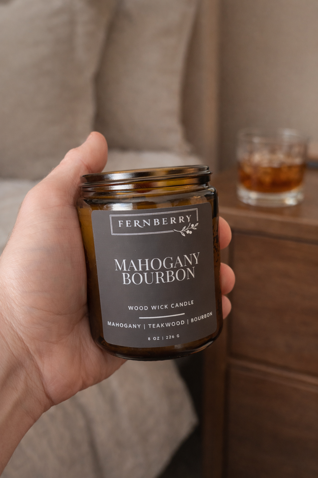 Hand holding a Fernberry Mahogany Bourbon candle with a blurred background