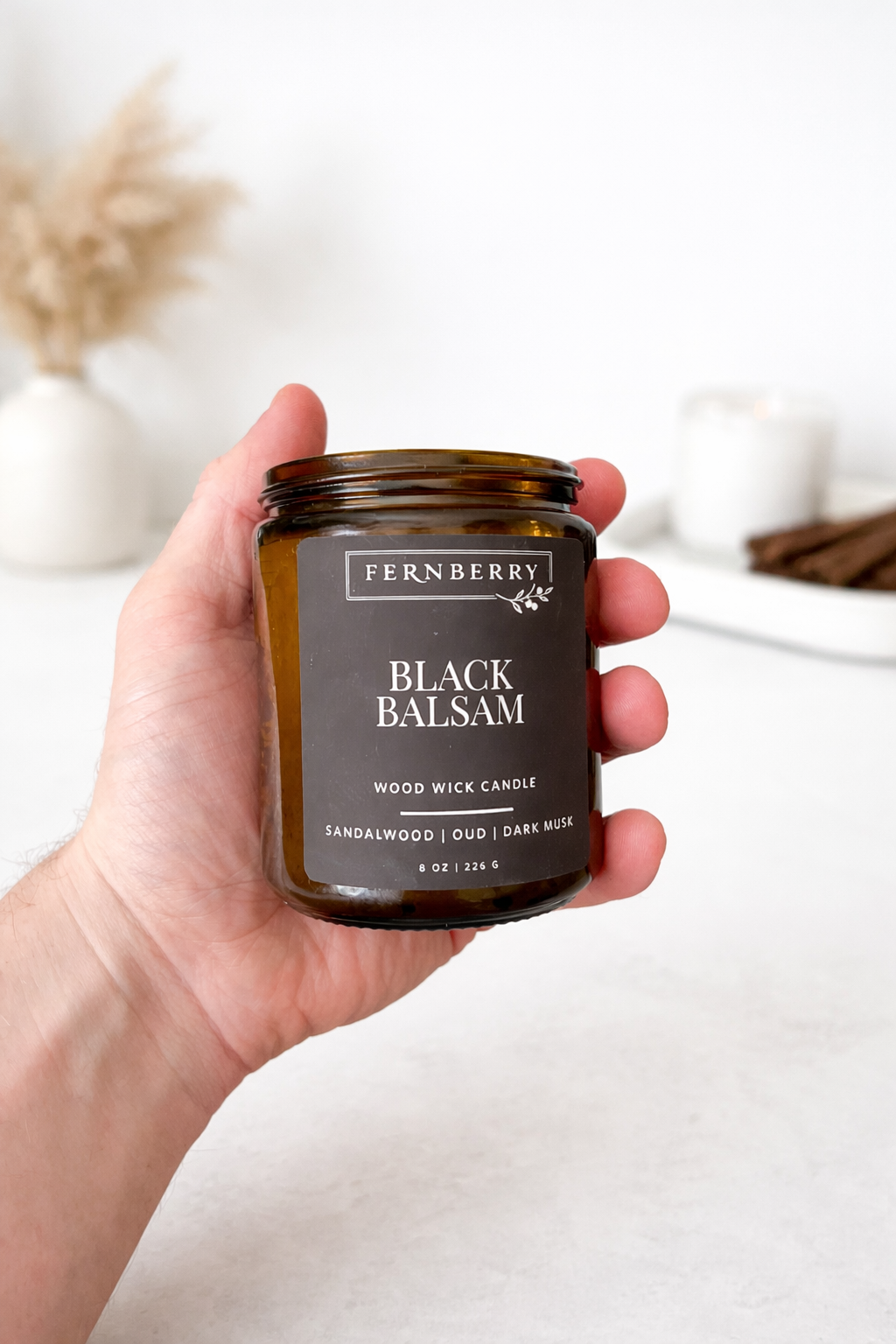 Hand holding a Fernberry Black Balsam candle against a neutral background