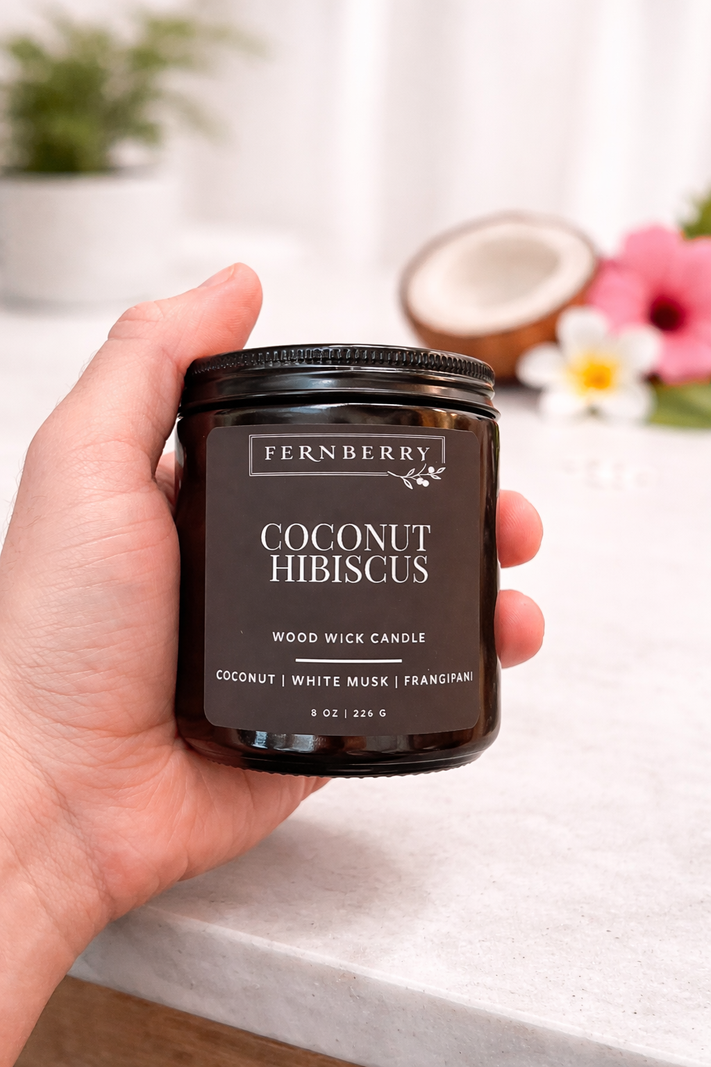 Hand holding a Fernberry Coconut Hibiscus candle with a blurred background