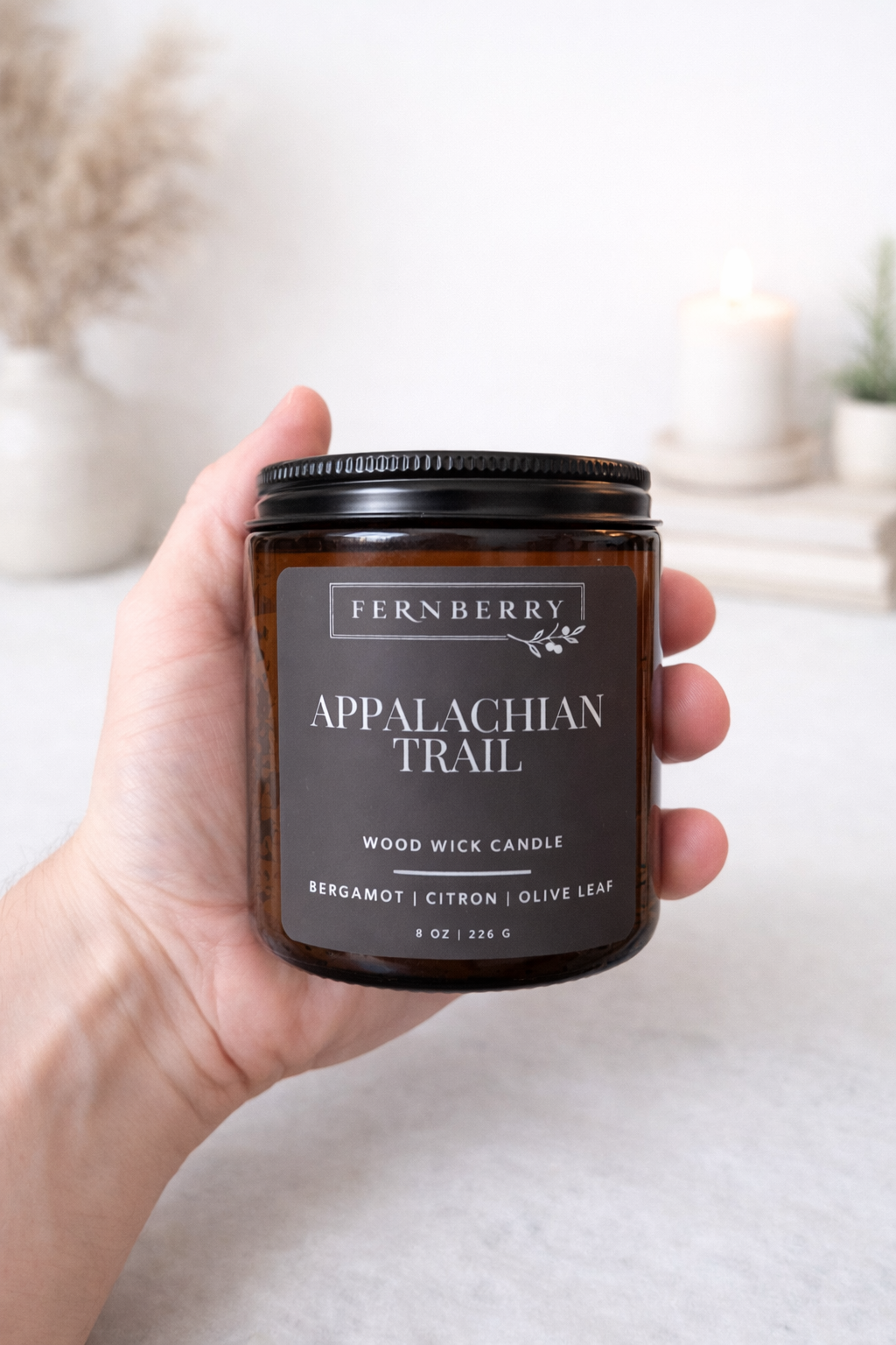 Hand holding a Fernberry Appalachian Trail candle against a blurred background