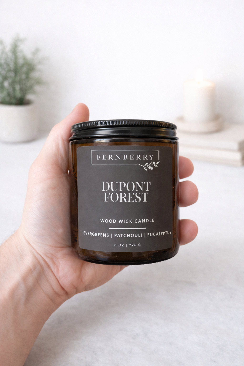 Fernberry Dupont Forest candle held in a hand with a neutral background