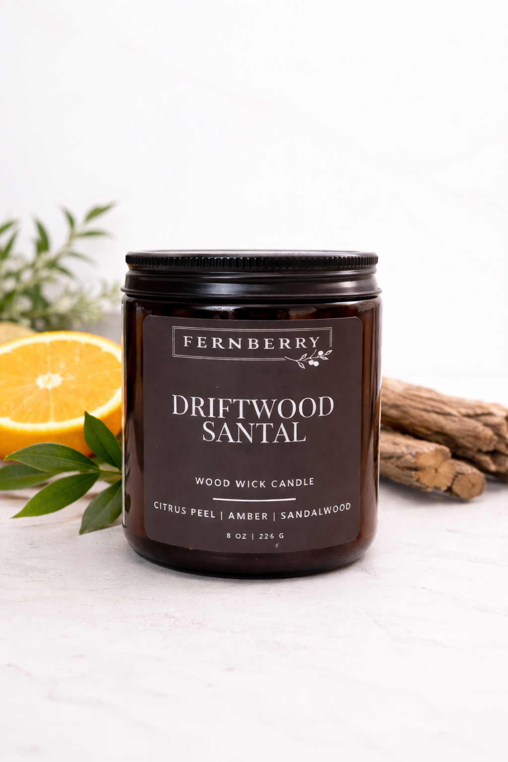 Fernberry Driftwood Santal candle with a lemon, sandalwood, and green leaves on a white background