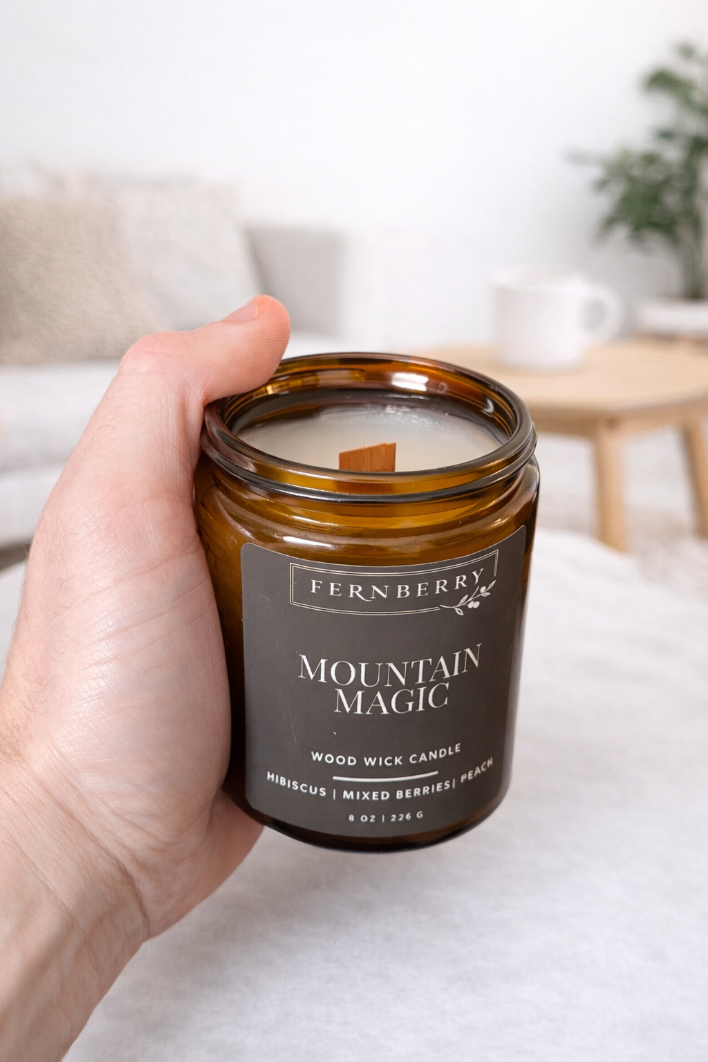 Hand holding a 'Mountain Magic' candle by Fernberry in a home setting