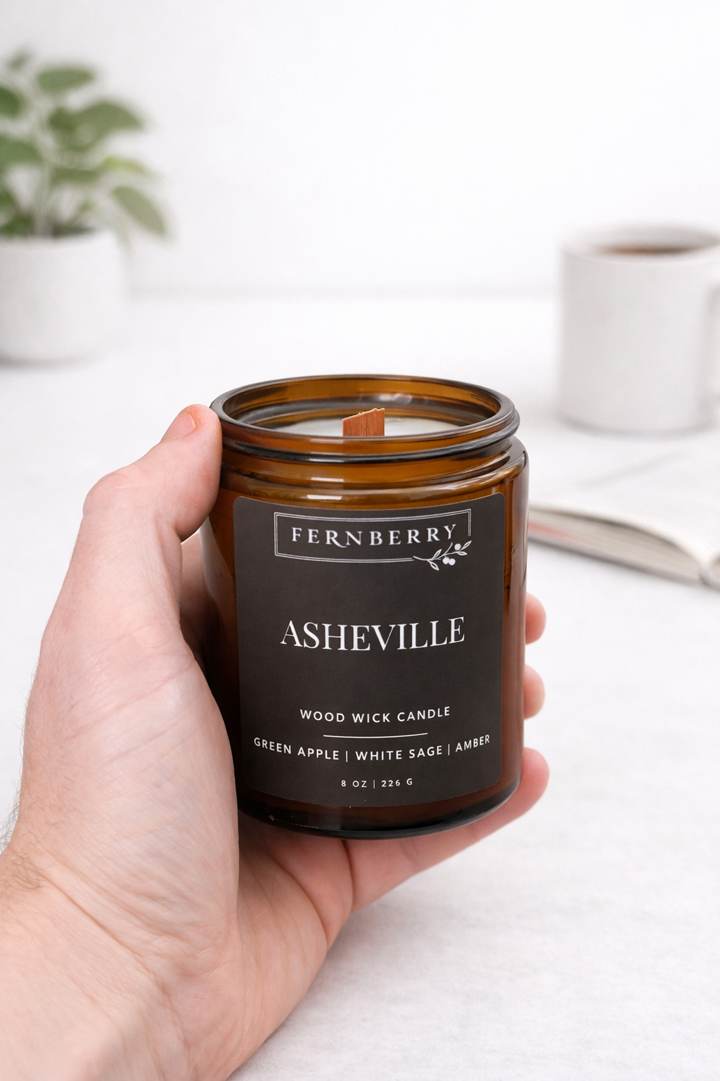 Hand holding a Fernberry Asheville candle with a blurred indoor background