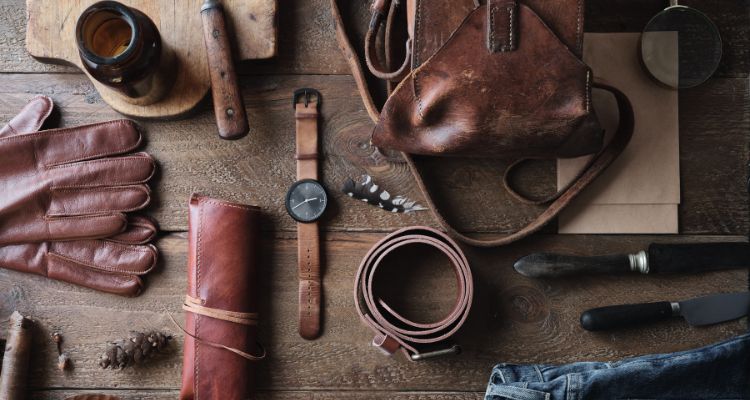 Collection of leather goods including a belt, watch, and gloves on a wooden surface.